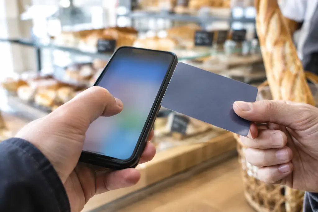 Un pouce touche un téléphone flou près d’une carte unie, devant une boulangerie.