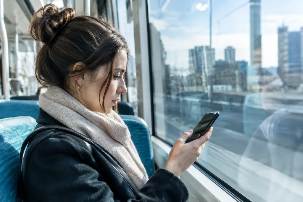Une passagère protège l’écran de son téléphone dans une rame de tram lumineuse.