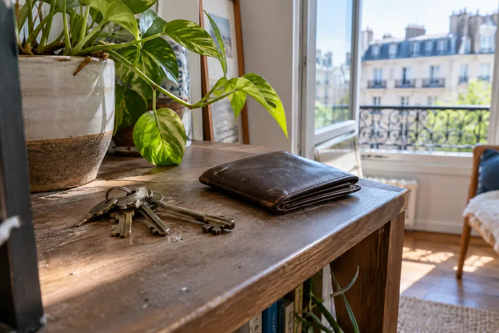 Un portefeuille fermé et un vieux trousseau de clés sur une étagère près d’une plante.