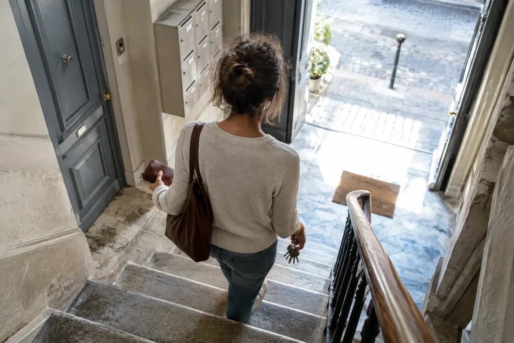 Une personne descend un escalier ancien avec un porte-monnaie et des clés.